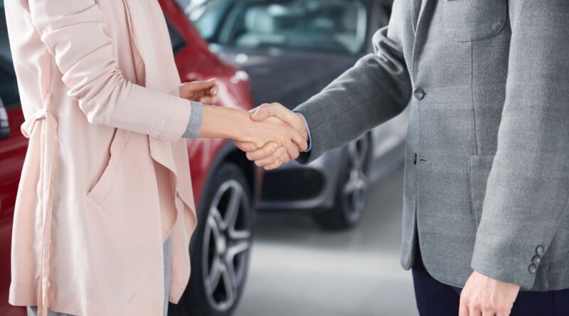 Homem e mulher apertam mãos na frente de carros